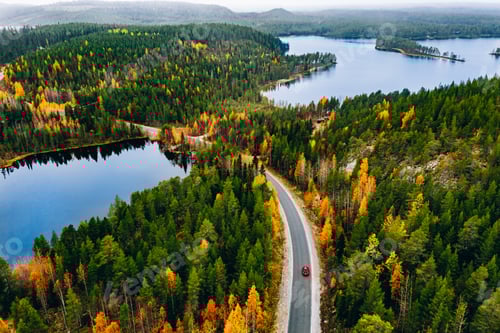Preview: Aerial view of rural road with red car in yellow and orange autumn forest with blue lake