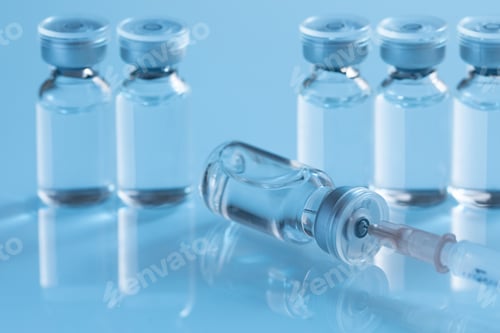 Preview: Closeup shot of covid19 vaccine bottles with a needle on a blue background - covid19 concept