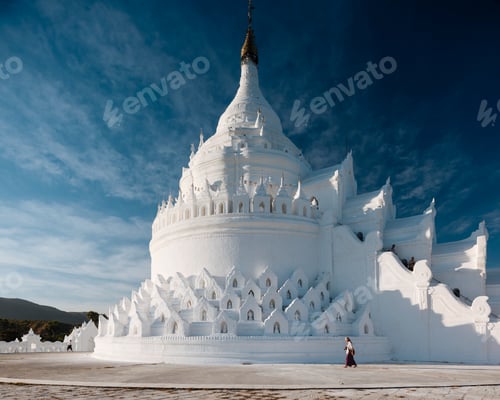 Preview: Woman walking by a large white pagoda under a blue sky.