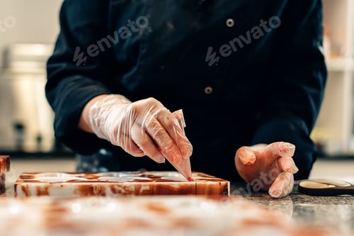 Preview: close up on hands of a pastry chef decorating white chocolates in an artisanal workshop