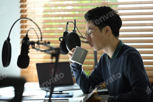 Preview: Young asian man radio host sitting front of condenser microphone and drinking hot coffee.