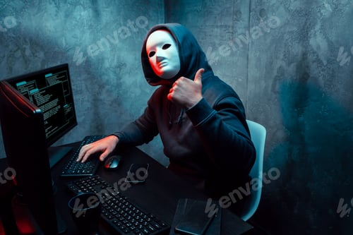 Hacker anónimo con máscara facial trabajando en una computadora en un cuarto oscuro