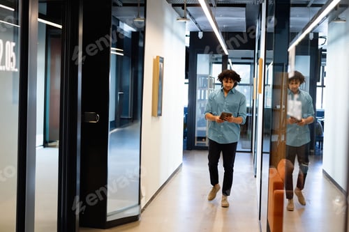 Preview: African American man in business attire walking down hallway carrying tablet by glass partition