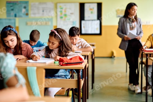 Preview: Hispanic schoolgirl and her classmates writing in the classroom.