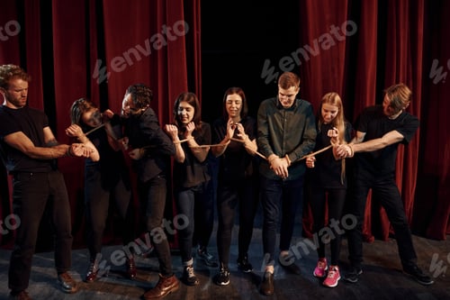 Preview: With rope in hands. Group of actors in dark colored clothes on rehearsal in the theater