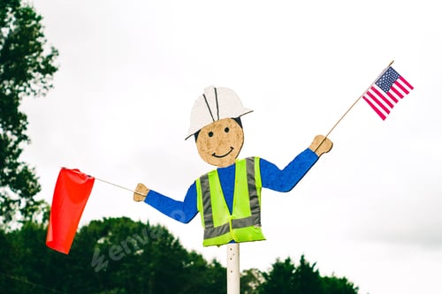 Preview: Cardboard sign of a man holding a red flag and a USA flag with trees in the background