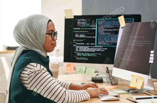 Preview: Young Muslim businesswoman in hijab looking at computer screen while typing