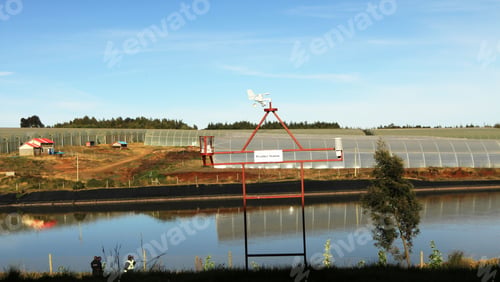 Preview: Reservoir with large greenhouses in the background in the daylight