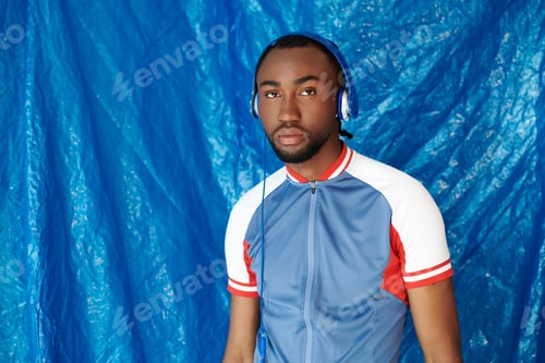 Preview: Charming young man with headphones poses confidently against a striking blue backdrop