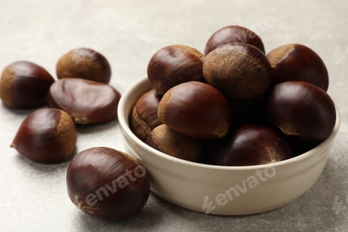 Preview: Bowl with roasted edible sweet chestnuts on light grey table, closeup
