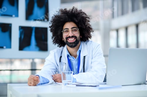 Preview: Portrait of cheerful male doctor sitting in hospital, looking at camera