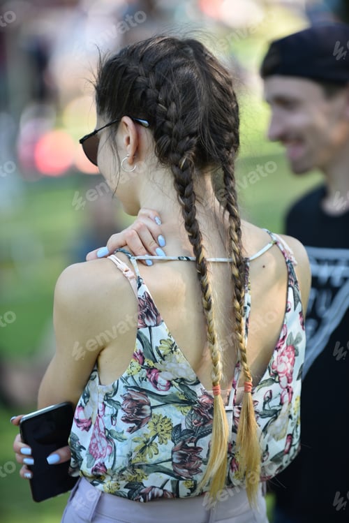 Preview: A young woman with a mobile phone in her hand and with long hair is standing in the back.