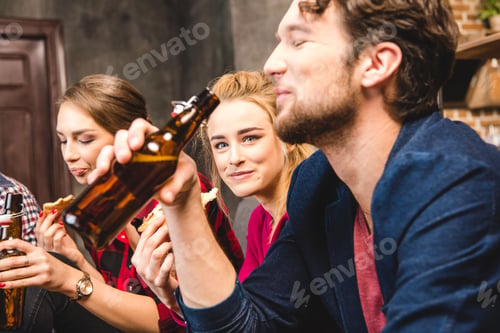 Preview: Smiling friends drinking beer while sitting on sofa