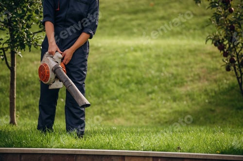 Preview: Leaf blower in hands, cleaning the way. Professional gardener is on the lawn