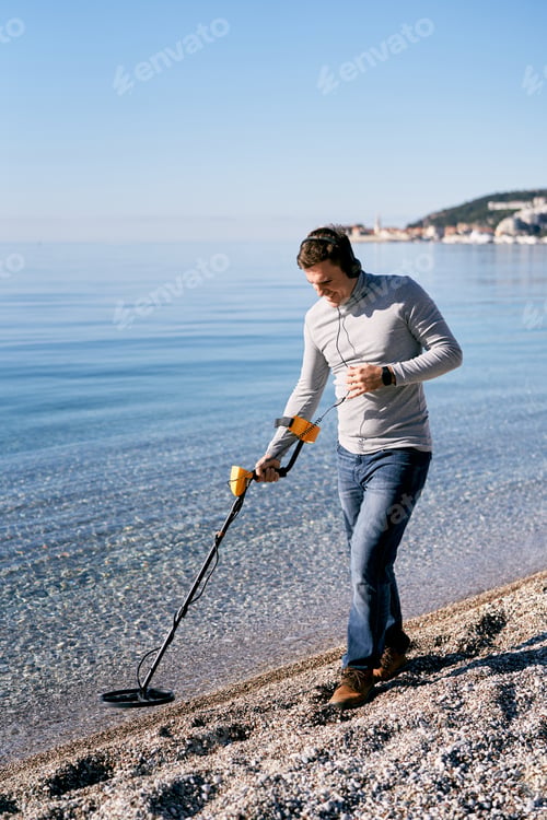 Preview: Man in headphones with a metal detector walks along the pebble beach