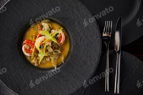 Preview: top view of delicious restaurant soup with shrimps in black plate with cutlery