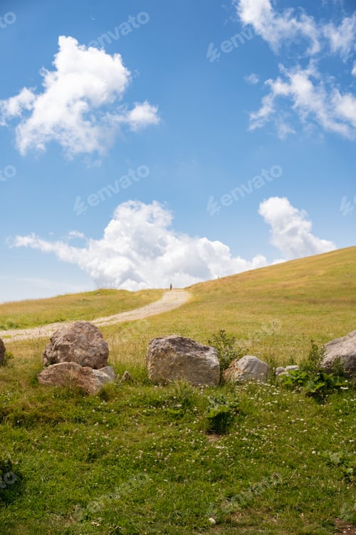 Preview: Landscape of green meadows between mountains, with a blue sky with clouds.