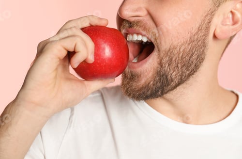 Preview: Young man with healthy teeth and apple on color background, closeup