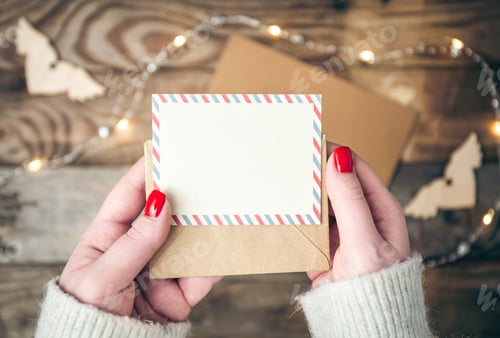 Preview: Blank postcard and envelope in female hands on a blurred wooden background.