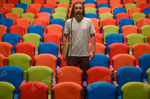 Preview: Man with dreadlocks standing in theatre with colorful seating