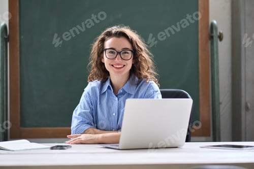Preview: Young happy female online teacher sitting at work desk with laptop. Portrait