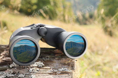Preview: Binoculars on wooden log outdoors. Mountain landscape reflecting in lenses