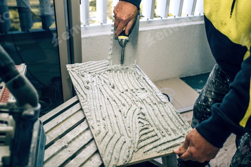 Preview: Professional builder smears cement glue on the ceramic tile with a trowel.