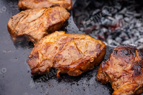 Preview: Grilled steaks on a round grill over coals, top view
