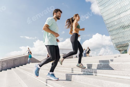 Preview: A man and a woman jog up stairs in an urban area under a bright sky, focused on their workout.