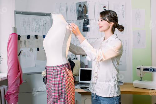 Preview: Female dressmaker working on new model tailoring pants on mannequin in studio.