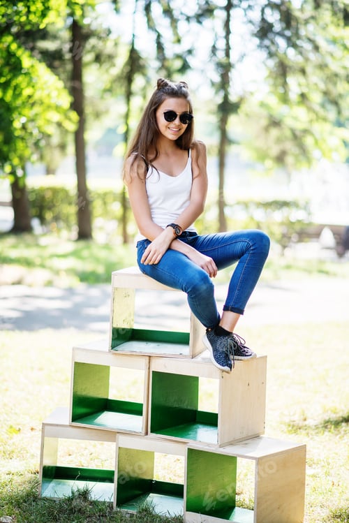 Preview: Portrait of a fashionably dressed girl posing on wooden boxes in the park on a sunny day