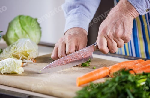 Preview: Cropped view of mature man chopping fresh vegetables for salad. Closeup of male hands.