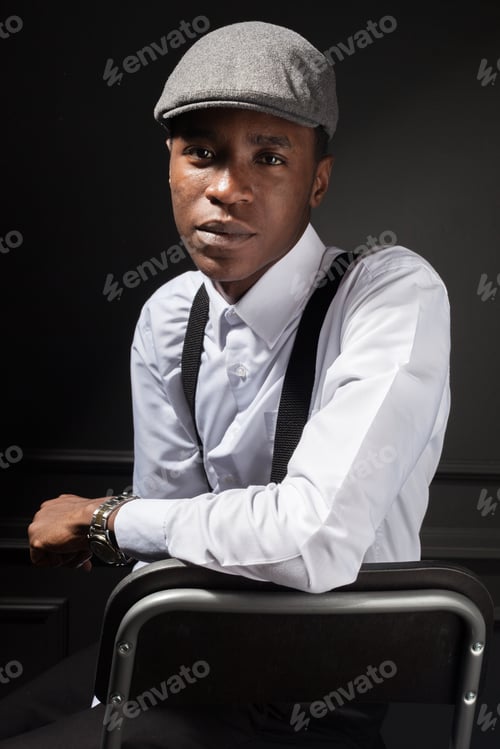 Preview: Young man in gray cap and shirt poses confidently on a chair in a dark setting