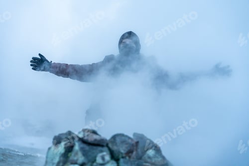 Preview: man walking behind the steaming fumaroles at Hverir or Namafjall geothermal park in winter, Iceland