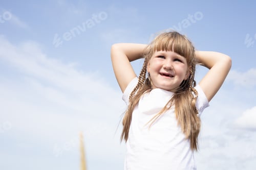 Preview: little girl of five years old in a white t-shirt on a background of blue sky, summer vacation
