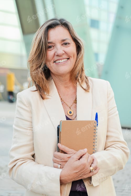 Visualização: Vertical. Empresária madura confiante olhando para a câmera enquanto segura um caderno e uma caneta