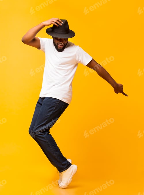 Preview: Young cheerful man dancing on tiptoes on yellow studio background