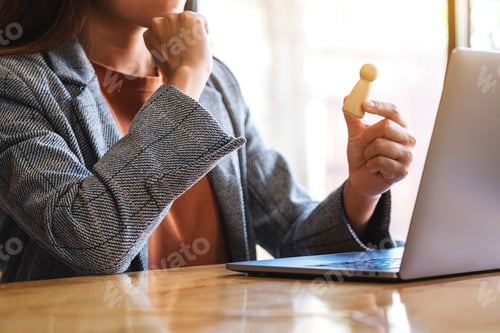 Preview: Businesswoman leader holding and choosing wooden people while working on laptop computer in office