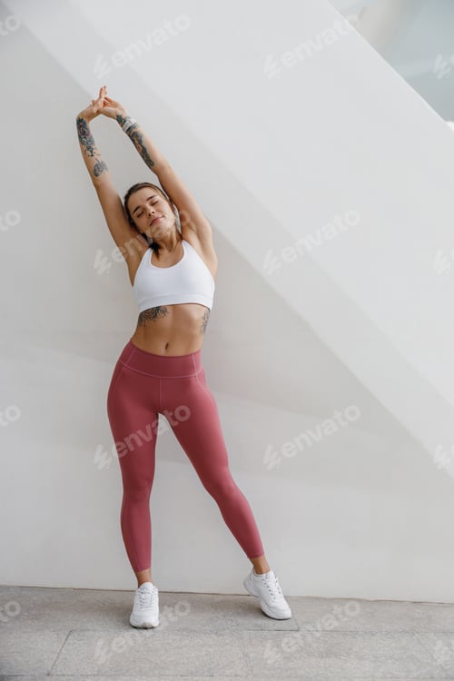 Preview: Young female athlete in tracksuit stretching outdoor and preparing to jogging. Healthy life concept