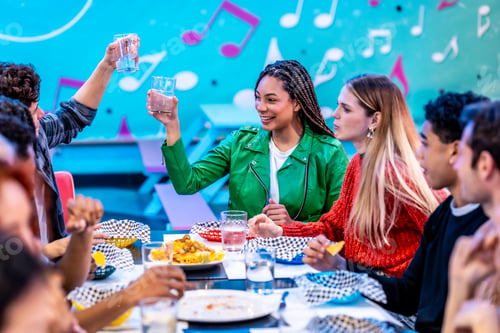 Preview: Group of diverse friends toasting drinks at bowling alley restaurant