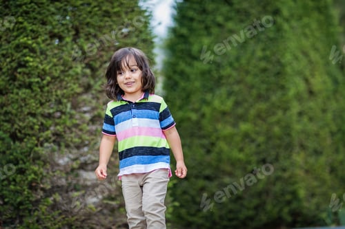 Preview: Handsome little boy walking among neatly trimmed trees in picturesque old park