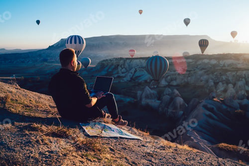 Preview: Male tourist with laptop looking at hot air balloons