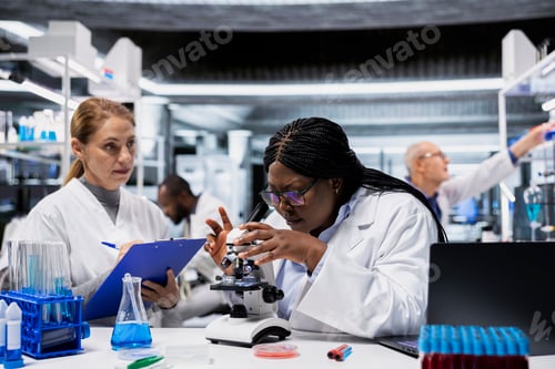 Preview: Female scientists examining bacterial cultures on slide using lab microscope