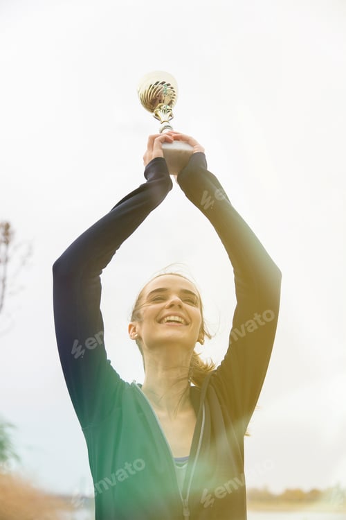 Preview: Happy sporty young woman holding gold trophy cup