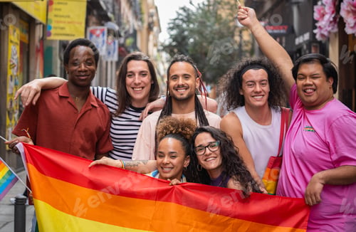 Preview: Group of happy LGBTQ people are posing with a rainbow flag before a gay parade MADO in Madrid city