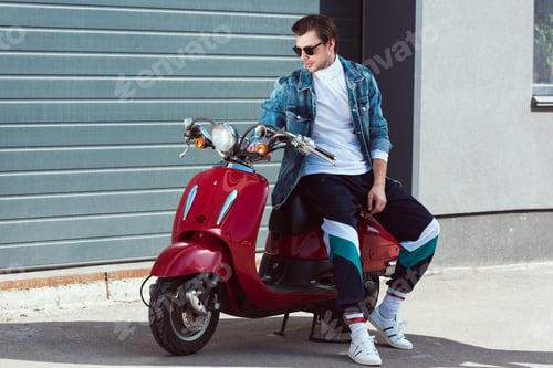 Preview: handsome young man in stylish vintage clothes sitting on scooter