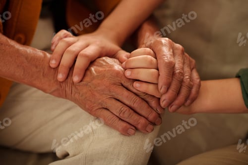Preview: Hands of senior woman in white linen pants holding those of granddaughter
