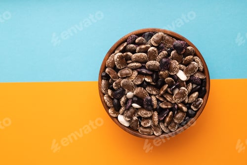 Preview: wooden bowl with Kidney beans on blue and orange pastel paper, top view, copy space
