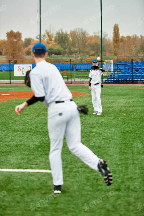 Preview: Two teenage boys enjoy baseball practice on a green field during a cloudy day