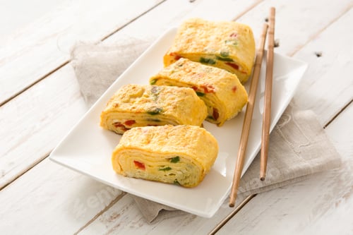 Preview: Tamagoyaki, japanese rolled omelette with chopsticks, resting on white plate
